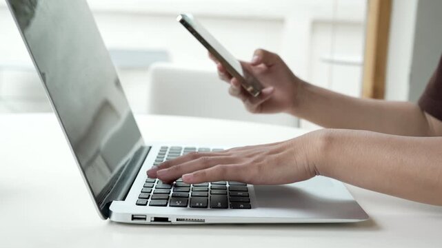 Close up man hands using smartphone and laptop computer for two factor authentication or multitasking. Business person working at office desk. Concept of digital technology, connection and finance