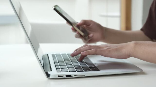 Close up man hands using smartphone and laptop computer for two factor authentication or multitasking. Business person working at office desk. Concept of digital technology, connection and finance