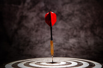 Dart arrow hitting the center of dartboard with red dart arrow