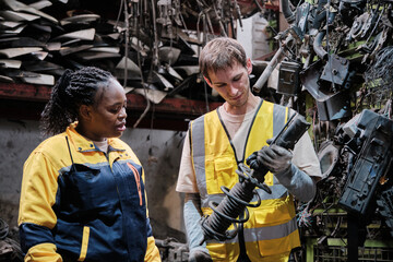 White male worker checks auto spare parts stock storage with Black female inspector at stack warehouse, working labor job in manufacturing factory, and industrial occupation for distribution business.