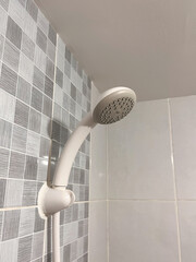 a white handheld shower head mounted on a wall bracket inside a bathroom.