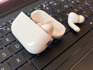 , close-up shot featuring a pair of modern white noise-canceling wireless earbuds. One earbud is placed inside its open charging case