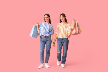 Fototapeta premium Beautiful young twin sisters with shopping bags on pink background