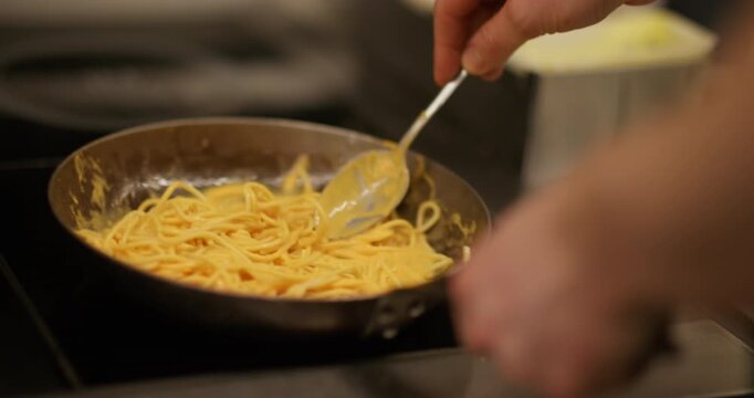 Cooking spaghetti. Noodle meal. Chef hand stirring hot vegetarian dish frying pan by metal spoon on stove. Tasty pasta in yellow sauce.