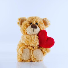Adorable teddy bear holding red heart on white background