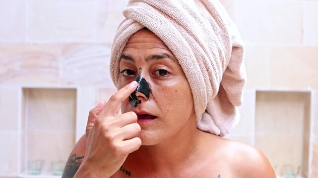 Woman with a towel applying blackhead remover mask on her nose