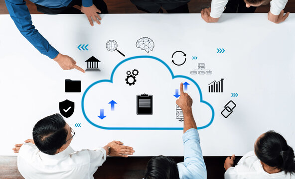 A group of business professionals collaborates around a table, focusing on cloud computing strategy. Various icons represent data management, analytics, and connectivity concepts. Trope - Powered by Adobe