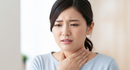 喉の痛みで辛そうな表情を浮かべ、首を手で押さえる若い女性