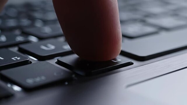 Extreme slow motion close-up shot of an isolated backlit black keyboard key gently pressing down against the metallic surface of a high-end laptop professional environment, metallic surface, concept