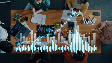 A diverse business team collaborates over a table, analyzing data and financial charts with laptops and notes in a modern office, showcasing teamwork and strategy. Scalp