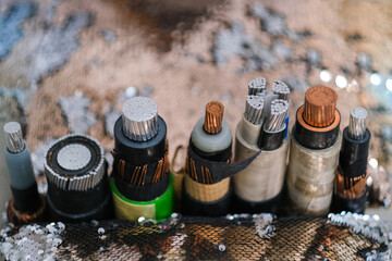 Several types of cut electrical cable showing layers of copper, aluminum, insulation, and protective sheathing for energy transmission.