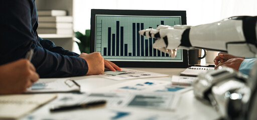 A dynamic office scene showcasing teamwork, where individuals collaborate with futuristic robotic technology and data analytics to drive business strategies effectively.Noogenesis