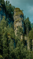 Obraz premium Tall rock formation surrounded by dense green trees under partly cloudy sky