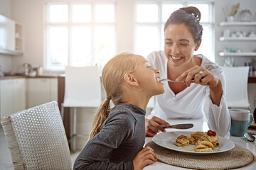 Mother, feeding and kid with food in kitchen for breakfast, pancakes meal and bonding together. Child, eating and woman with flapjacks for morning snack, family nutrition and brunch dessert at house