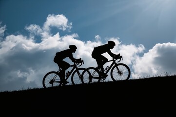 Obraz premium Inspirational fitness image of bike riders pushing limits on mountain terrain against moody overcast sky backdrop.