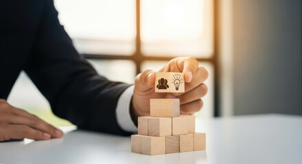 A man in a suit holds a wooden block on top of stacked blocks on a table in an office.