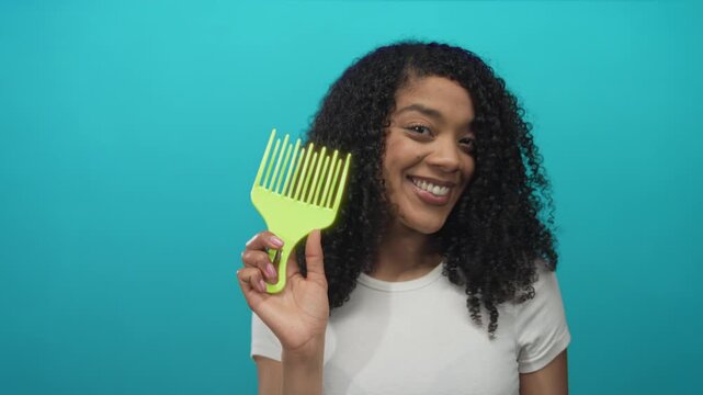 African american woman points finger at green hair pick while smiling in studio; confidence selfcare.