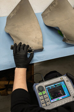 Technician conducting non-destructive ultrasonic inspection of aeroplane turbine fan blades with portable testing device, displaying scan results on digital screen during maintenance procedure
