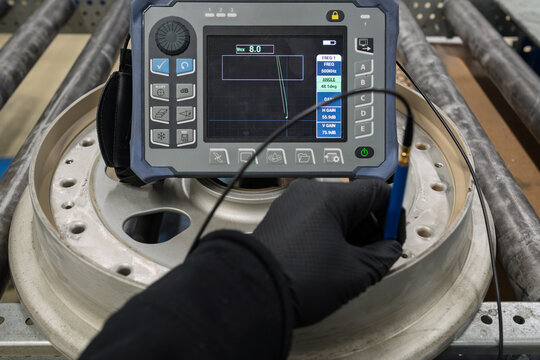 NDT inspector conducting eddy current testing on an aircraft landing gear wheel using a handheld NDT instrument with a digital display showing crack indication during aerospace component evaluation
