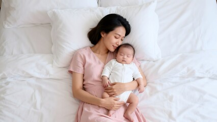 Mother holding sleeping baby on bed