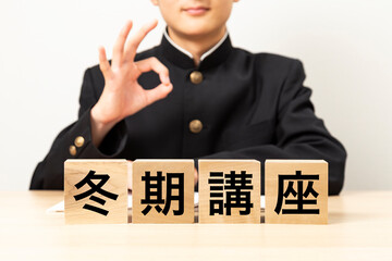 「冬期講座」と書かれたブロックとOKサインをする男子学生
