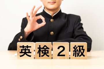 「英検2級」と書かれたブロックとOKサインをする男子学生