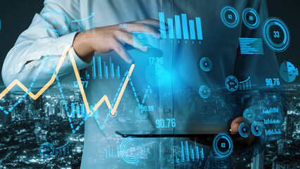 A businessman utilizes a tablet to analyze financial data, showcasing graphs and charts that illustrate market trends against a cityscape backdrop at night. Xenic