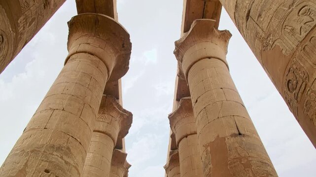 Low-angle view of massive ancient stone columns carved with hieroglyphs, forming monumental corridor inside an Egyptian temple complex. Temple of Amun-Ra, Luxor, Egypt. UNESCO World heritage site