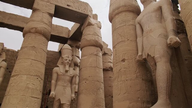 Panning footage showing ancient Egyptian temple featuring massive stone columns and colossal standing statues carved in high relief. Temple of Amun-Ra, Luxor, Egypt. UNESCO World heritage site
