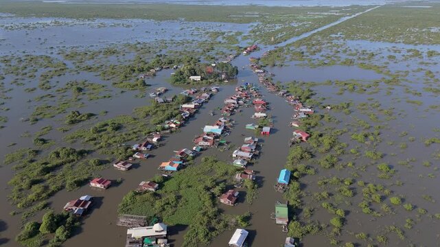 Mechrey, true floating rural village on the shores of Tonle Sap lake nestled among mangroves with man made channel in background. Aerial drone fly over.
