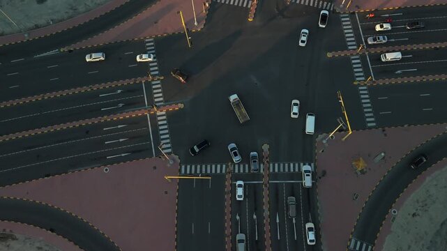Top-down drone over a busy multilane intersection at golden hour&mdash;cars, zebra crossings, and crisp lane markings forming a geometric city-grid pattern with long shadows in a Gulf-region urban setting.