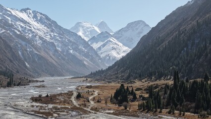 Stunning mountain landscape featuring snow-capped peaks under clear blue sky, with a winding river...
