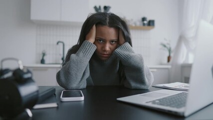 Frustrated and exhausted freelance at home office, portrait of black woman. Female worker or student sitting at table with laptop in kitchen and holding head, feel headache and tiredness, online job - Powered by Adobe