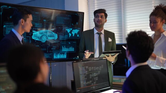 Diverse group of business professionals sitting in a row in a dark high-tech room. Two men and two women holding laptops and tablets while looking forward at a digital presentation screen. The scene r