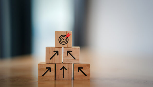 Business growth concept with hand stacking wooden blocks upward, showing arrows and target icon. Represents strategy, goal achievement, development, planning, leadership, and long-term success. 