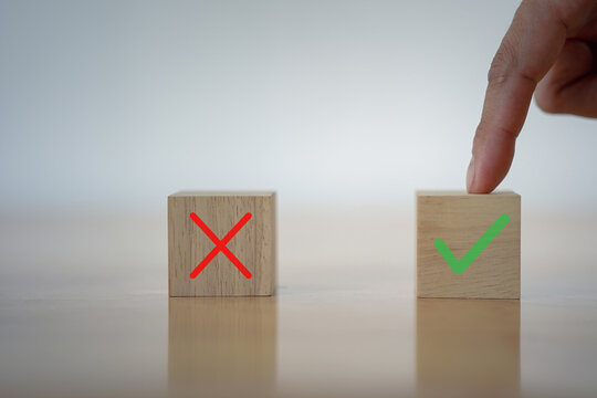 Hand selecting a wooden block with a green check mark among red cross blocks, symbolizing correct choice, decision making, quality control, and choosing the right option in business or personal tasks.
