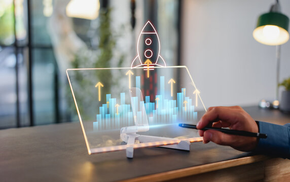 Startup business growth concept. Businessman pointing at rising bar graph with rocket icon, percentage sign and upward arrows, symbolizing success, investment return, and financial innovation.