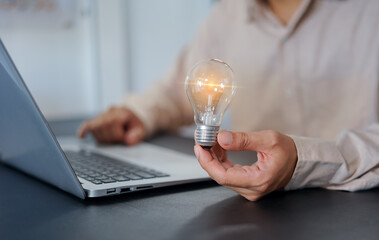 Businessman holding a light bulb and a laptop representing business success and technology ideas in the office