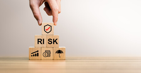 Risk management concept with hand placing shield icon block on stacked wooden cubes showing finance, growth, and protection symbols, representing business strategy, financial planning, risk control