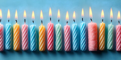 A colorful array of lit birthday candles with a gentle spiral design stand side by side on a soft blue background ready for celebration.