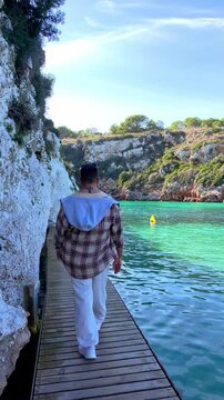 Man walking on wooden boardwalk at Es Canutells beach, Menorca.