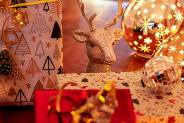 Atmospheric, festive Christmas decoration with a glittering reindeer figure, wrapped gifts, and glowing star balls on a wooden surface.