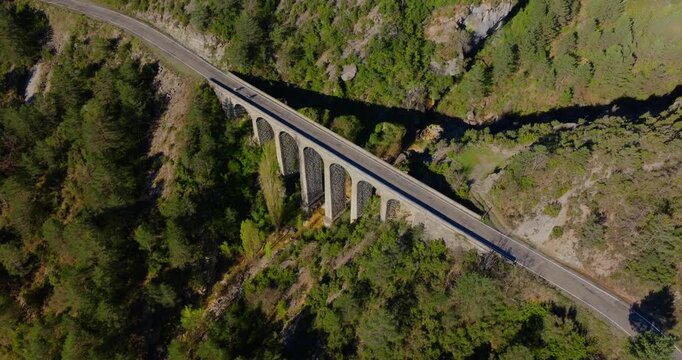 Slow descending drone reveals cyclists riding across stone arch viaduct over R&iacute;o Cinca gorge on the HU‑641 mountain road linking Mirador de Fuebla to A&iacute;nsa in Huesca, Aragon, Spain.