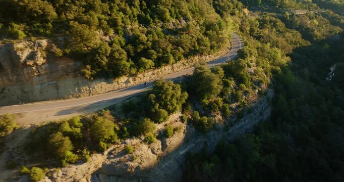 Lateral drone tracking sequence follows two cyclists along a high-altitude ledge road near Ainsa, where the golden hour sun rakes across the layered limestone cliffs of the Spanish Pyrenees.