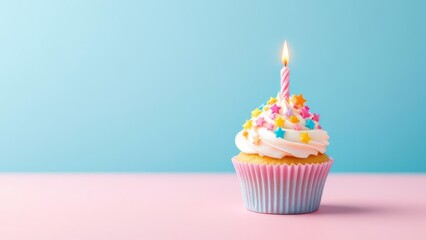 Pastel birthday cupcake with candle and colorful sprinkles on soft pink surface and blue background. Minimal festive dessert concept with copy space, perfect for celebration, greeting, and party desig
