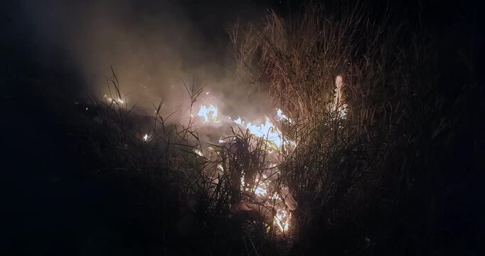 Close up of flames consuming plastic and grass at night.