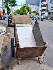 Simple manual transportation vehicle made of plywood panels standing on the side of a busy road in Vietnam