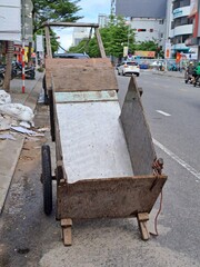 Simple manual transportation vehicle made of plywood panels standing on the side of a busy road in Vietnam