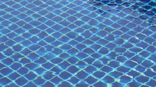 Blue pool tiles appear beneath rippling water with light reflections, filling the frame with repeating grid patterns and a clean geometric surface.