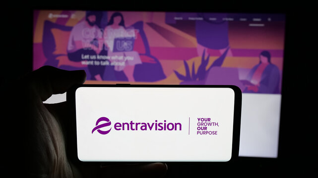 Stuttgart, Germany - 12-11-2025: Person holding cellphone with logo of US company Entravision Communications Corp. on screen in front of webpage. Focus on phone display.